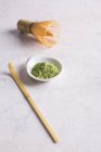 Green matcha tea powder and bamboo whisk with spoon on table. — Stock Photo