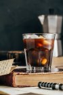 Cold espresso coffee in glass on dark grunge background with antique book — Stock Photo