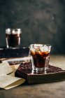 Cold espresso coffee in glass on dark grunge background with antique book — Stock Photo