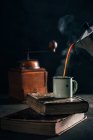 Poring café quente na xícara de esmalte em velhos livros rasgados no fundo escuro — Fotografia de Stock
