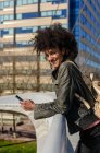 Femme aux cheveux afro regardant son téléphone en marchant sur un pont dans une ville — Photo de stock