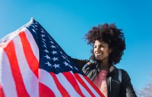 Mujer negra con el pelo afro y una bandera americana celebrando el día de la independencia de EE.UU. - foto de stock