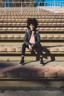 Black woman with afro hair sitting on the steps of a stadium — Stock Photo