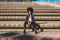 Чорна жінка з афро волоссям сидить на сходах стадіону — стокове фото