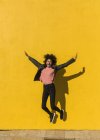 Donna nera con capelli afro che salta per la gioia in strada con un muro giallo sullo sfondo — Foto stock