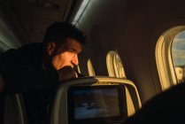 Seitenansicht eines erwachsenen Mannes, der aus dem Fenster eines modernen Flugzeugs blickt und während des Fluges denkt — Stockfoto