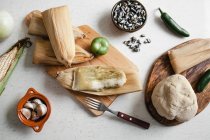 From above soft dough and corn husks lying near garlic and pepper for tamales on white tabletop — Stock Photo