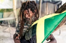Varón barbudo afroamericano con rastas sosteniendo bandera de Jamaica cerca del árbol - foto de stock
