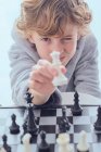 Menino mostrando figura de xadrez perto do tabuleiro — Fotografia de Stock
