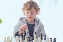 Niño sosteniendo figura en tablero de ajedrez - foto de stock