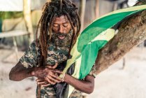 Varón barbudo afroamericano con rastas sosteniendo bandera de Jamaica cerca del árbol - foto de stock