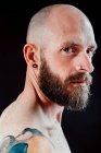 Side view of bald thoughtful hipster with earring and piercing looking away on black background — Stock Photo