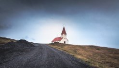 Beau bâtiment d'église situé près de la route de campagne rugueuse contre le ciel nuageux en Islande — Photo de stock