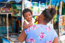 Back view of African American mother holding little kid near small souvenir shop in Jamaica — Stock Photo