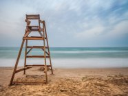 Cadeira salva-vidas na costa arenosa perto do mar ondulando contra o céu nublado — Fotografia de Stock