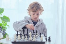 Niño sosteniendo figura en tablero de ajedrez - foto de stock