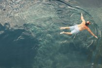 Von oben Rückansicht eines Mannes in kurzen Hosen, der in sauberem, blauem Wasser schwimmt — Stockfoto