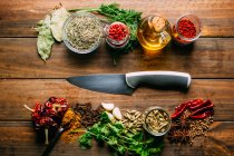 From above various spices and bottle of oil placed on timber tabletop near sharp knife — Stock Photo
