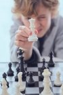 Funny child holding white chess figure near chess board on blurred background — Stock Photo
