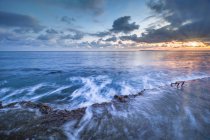 Strahlende Sonne am wolkenverhangenen Himmel über dem wunderschönen Meer, das in der Nähe der rauen steinigen Küste in der Natur winkt — Stockfoto