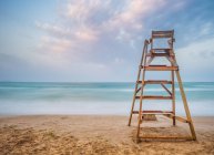 Рятівник стілець на піщаному березі біля махаючого моря проти хмарного неба — стокове фото