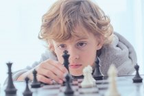 Мальчик держит фигуру на шахматной доске — стоковое фото