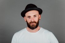 Бородатый хипстер в футболке и шляпе на черном фоне — стоковое фото