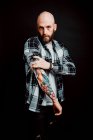 Bearded hairless hipster in shirt with tattoos on arms on black background — Stock Photo