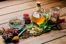 Разнообразные специи и травы и бутылка масла на деревянной столешнице — стоковое фото