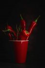 Свежий красный острый перец чили в чашке на черном фоне — стоковое фото