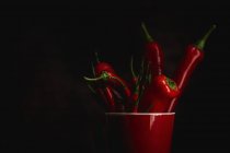 Fresh red spicy chilli peppers in cup on black background — Stock Photo
