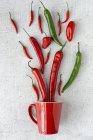 Fresh red and green spicy chilli peppers on white background with mug — Stock Photo