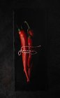 Fresh red spicy chilli peppers tied with twine on slate on black background — Stock Photo