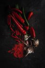 Frische rote und grüne Chilischoten, Knoblauchzehen und Gewürze auf schwarzem Hintergrund — Stockfoto