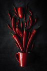 Fresh red spicy chilli peppers and mug on black background — Stock Photo