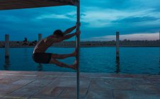 Молодой спортсмен без рубашки балансирует на полюсе у воды вечером — стоковое фото