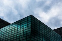 Desde abajo del exterior del edificio de vidrio con diseño futurista de vidrio bajo el cielo nublado - foto de stock