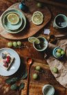 De cima de chapas cerâmicas bonitas e xícaras com partes de limão e uvas na composição na mesa de madeira — Fotografia de Stock