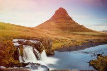 Landscape of beautiful waterfalls in long exposure on coast of river with green mountain peak on background, Iceland — Stock Photo