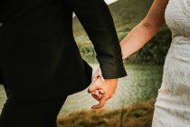 Faceless man and woman wearing wedding garments and holding hands while walking on coastline — Stock Photo