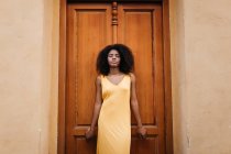 Verträumte schwarze Frau in gelbem Kleid lehnt an Tür auf der Straße — Stockfoto