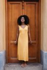 Dreamy black woman in yellow dress leaning on door on street — Stock Photo