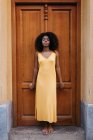Sonhador mulher negra em vestido amarelo inclinando-se na porta na rua — Fotografia de Stock