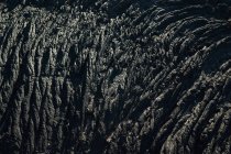 Closeup texture of dark rough rock in sunlight — Stock Photo