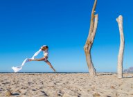 Vista laterale di attraente donna che salta con pareo sulla spiaggia di sabbia locanda soleggiata giornata nuvolosa — Foto stock