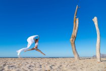 Вид збоку приваблива жінка стрибає з парео на піщаному пляжі в готелі сонячний безхмарний день — стокове фото