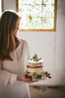 Souriant femme tenant assiette avec gâteau décoré par des fleurs et p — Photo de stock