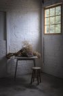 Buquê de galhos de coníferas secas em papel artesanal na mesa em quarto cinza escuro com paredes de tijolo — Fotografia de Stock