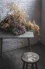 Buquê de galhos de coníferas secas em papel artesanal na mesa em quarto cinza escuro com paredes de tijolo — Fotografia de Stock