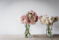 Mesa de madeira com buquês de flores frescas em vasos perto da parede branca — Fotografia de Stock